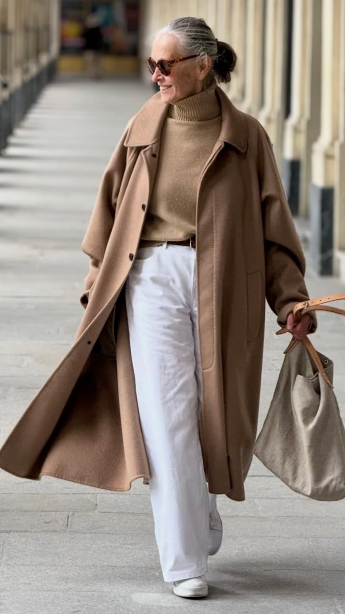 Look hiver femme 60 ans avec manteau long camel, pull col roulé beige, pantalon blanc et baskets blanches