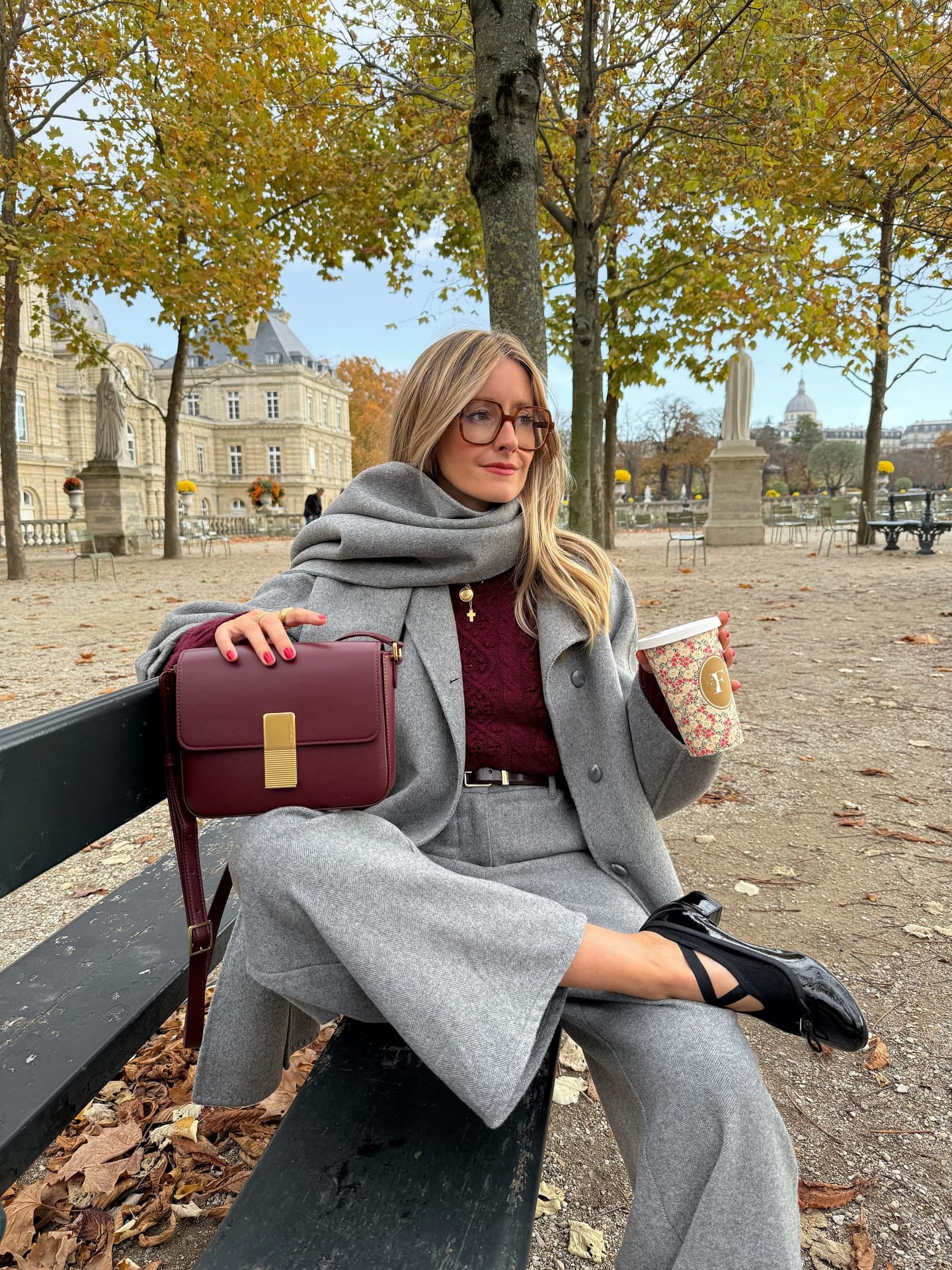 Manteau gris à écharpe intégrée avec tailleur et sac bordeaux, look d’hiver élégant au parc