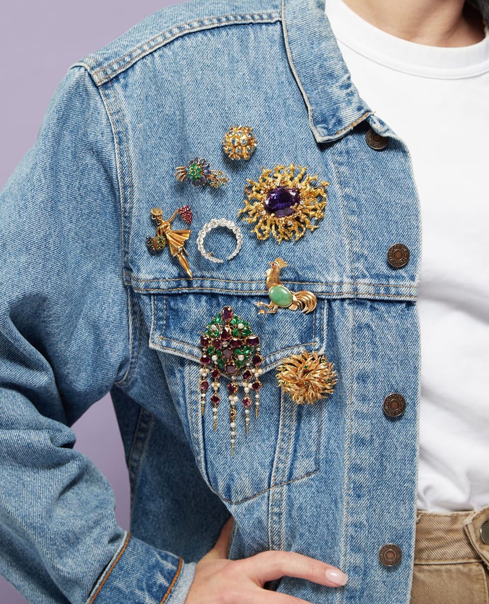 Accumulation de broches vintage dorées et ornées de pierres colorées épinglées sur une veste en jean