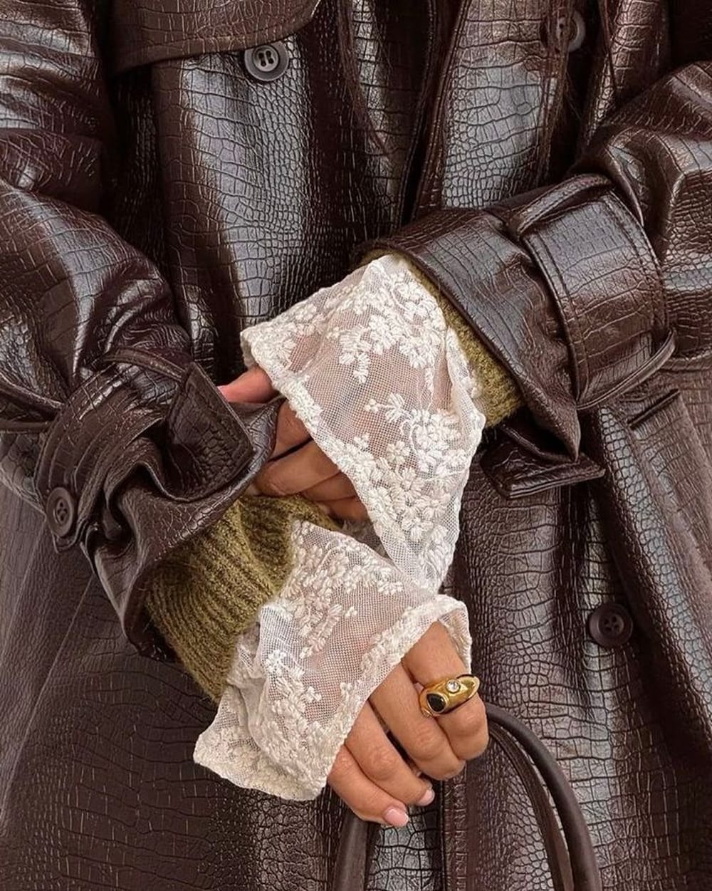 Manchette en dentelle blanche qui dépasse d'un pull kaki sous un manteau en cuir croco chocolat