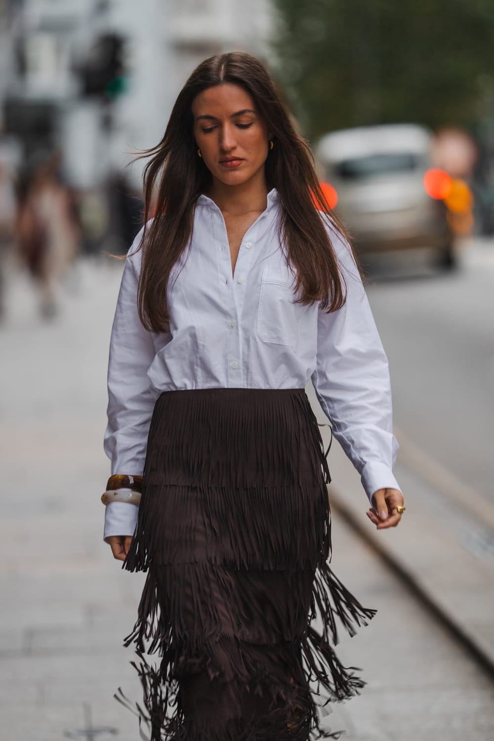 Jupe midi à franges superposées en daim chocolat portée avec une chemise blanche oversize, look tendance printemps