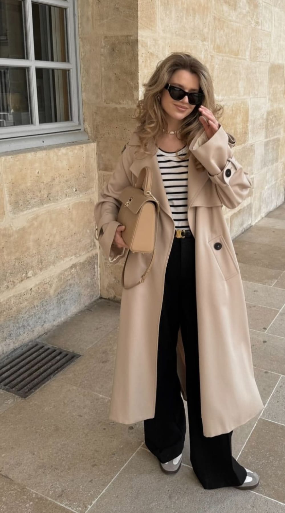 Look trench femme beige long porté ouvert avec marinière, pantalon noir large et sac nude