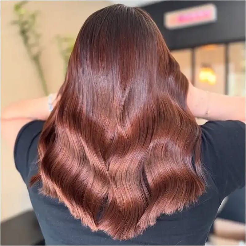 Coloration burnt sienna aux reflets cuivrés et bronzés réalisée en balayage sur cheveux mi-longs ondulés