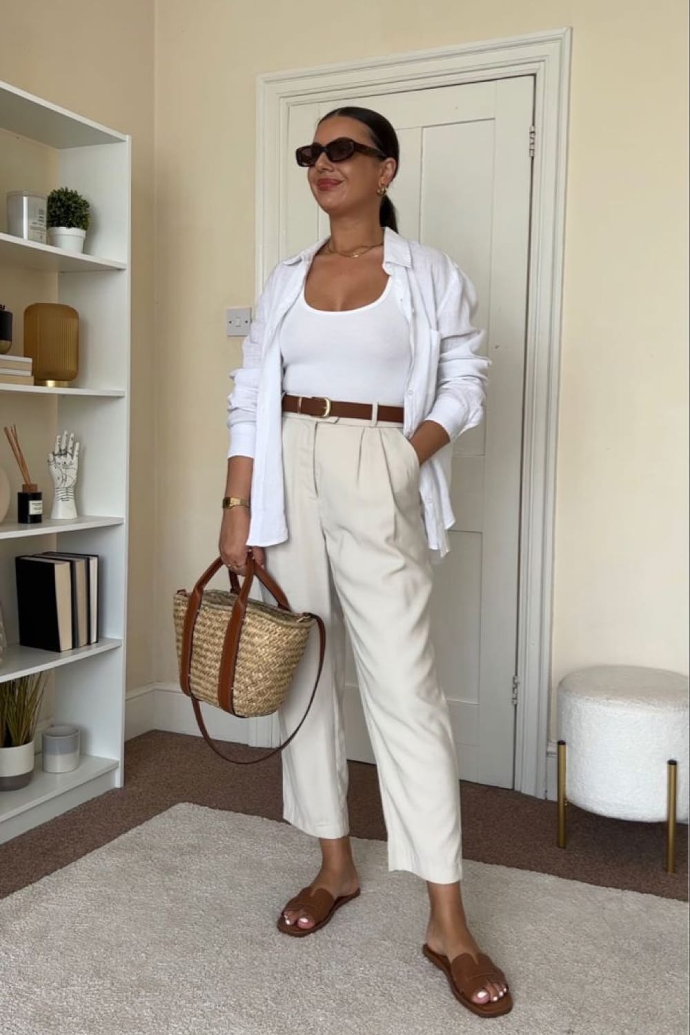 Mules plates en cuir camel portées avec un pantalon crème, un top blanc et un sac en paille