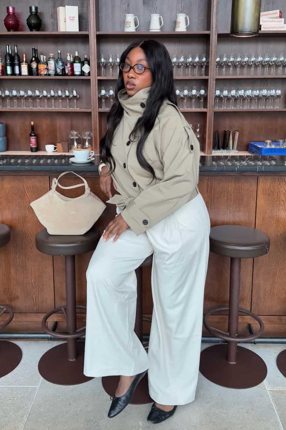 Trench court beige à col cheminée avec pantalon large blanc cassé et chaussures plates noires, tendance printemps 2026