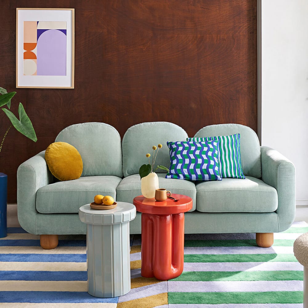 Canapé 3 places en velours eucalyptus avec dossiers arrondis et pieds cylindriques en bois clair, dans un salon coloré