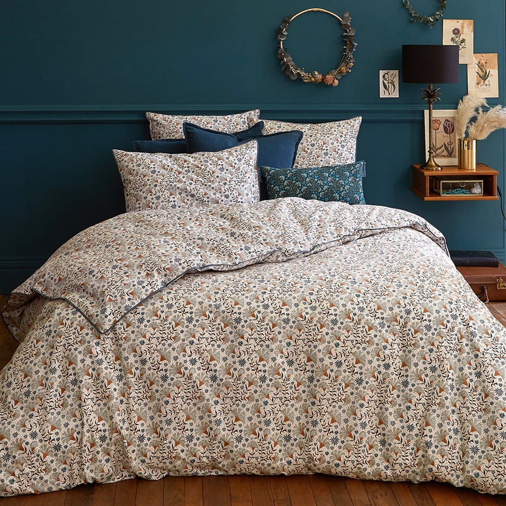 Housse de couette en percale de coton Kalyan avec imprimé fleuri bleu et terra cotta, sur un lit dans une chambre aux murs bleu canard