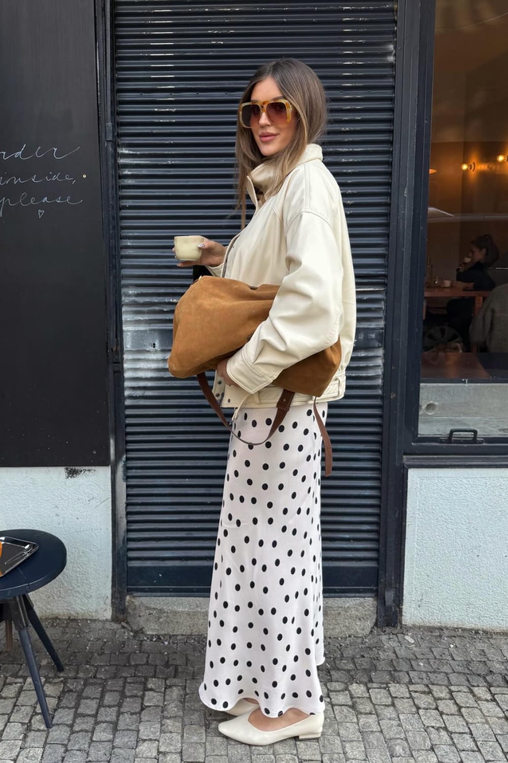 Look street style avec une jupe longue à pois noirs et blancs, veste en cuir écru oversize, sac cabas camel en daim et ballerines blanches