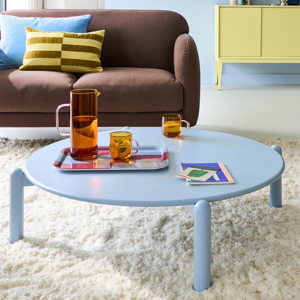 Table basse Talma avec plateau laqué bordeaux brillant et pieds en cannage naturel, dans un salon lumineux