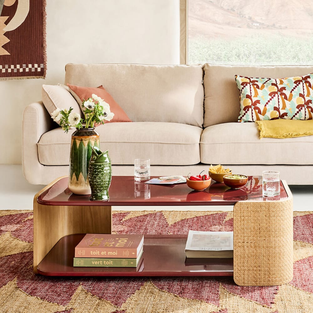 Table basse Talma avec plateau laqué bordeaux brillant et pieds en cannage naturel, dans un salon lumineux