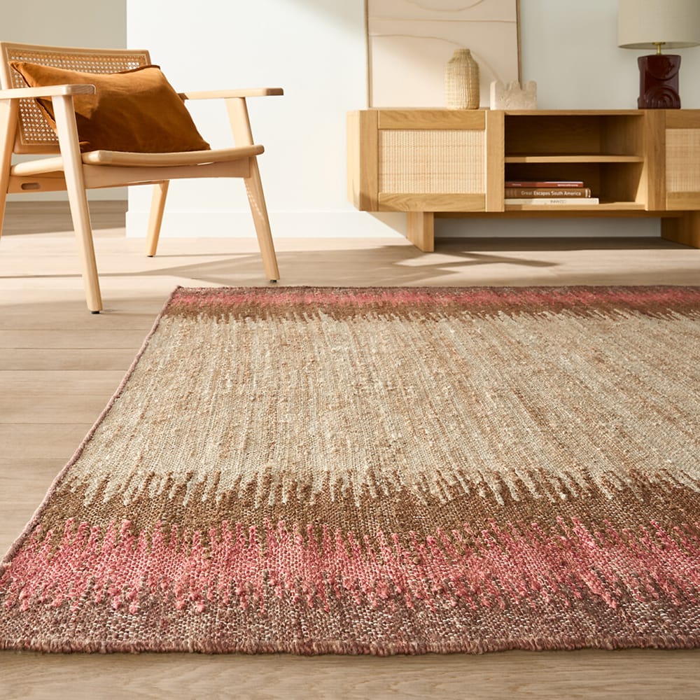 Tapis en jute tressé à la main Ikat avec motif dégradé rose et naturel, dans un salon aux tons chauds