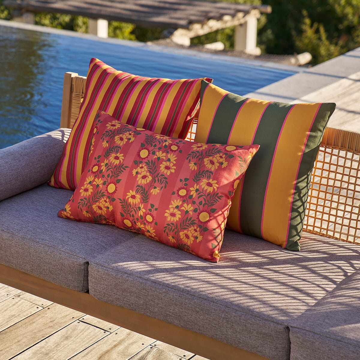 Coussins d'extérieur à fleurs et à rayures colorées posés sur un canapé de jardin au bord d'une piscine