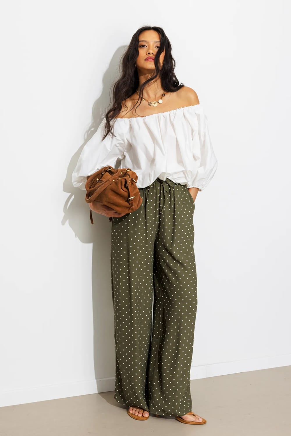 Look pantalon à pois kaki porté avec une blouse blanche épaules dénudées, un sac seau en daim et des sandales plates