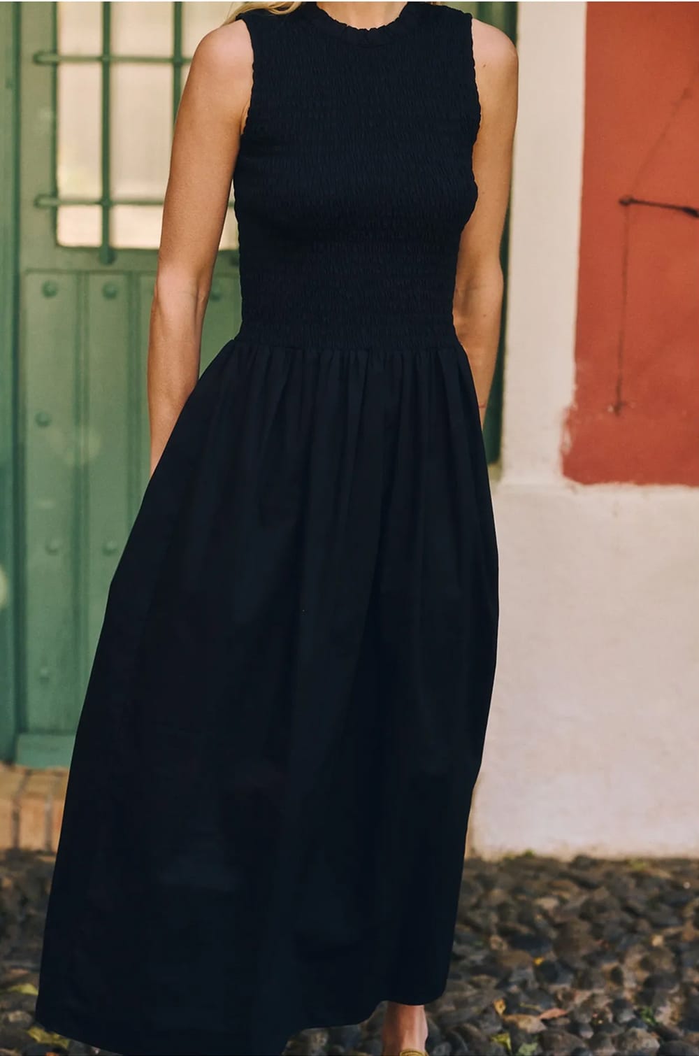 Robe noire sans manches à buste smocké et jupe longue fluide, portée en extérieur