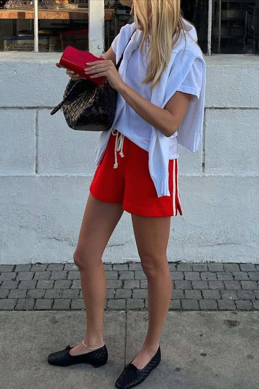 Short de sport rouge porté avec t-shirt blanc et cardigan pour un look sporty chic d'été