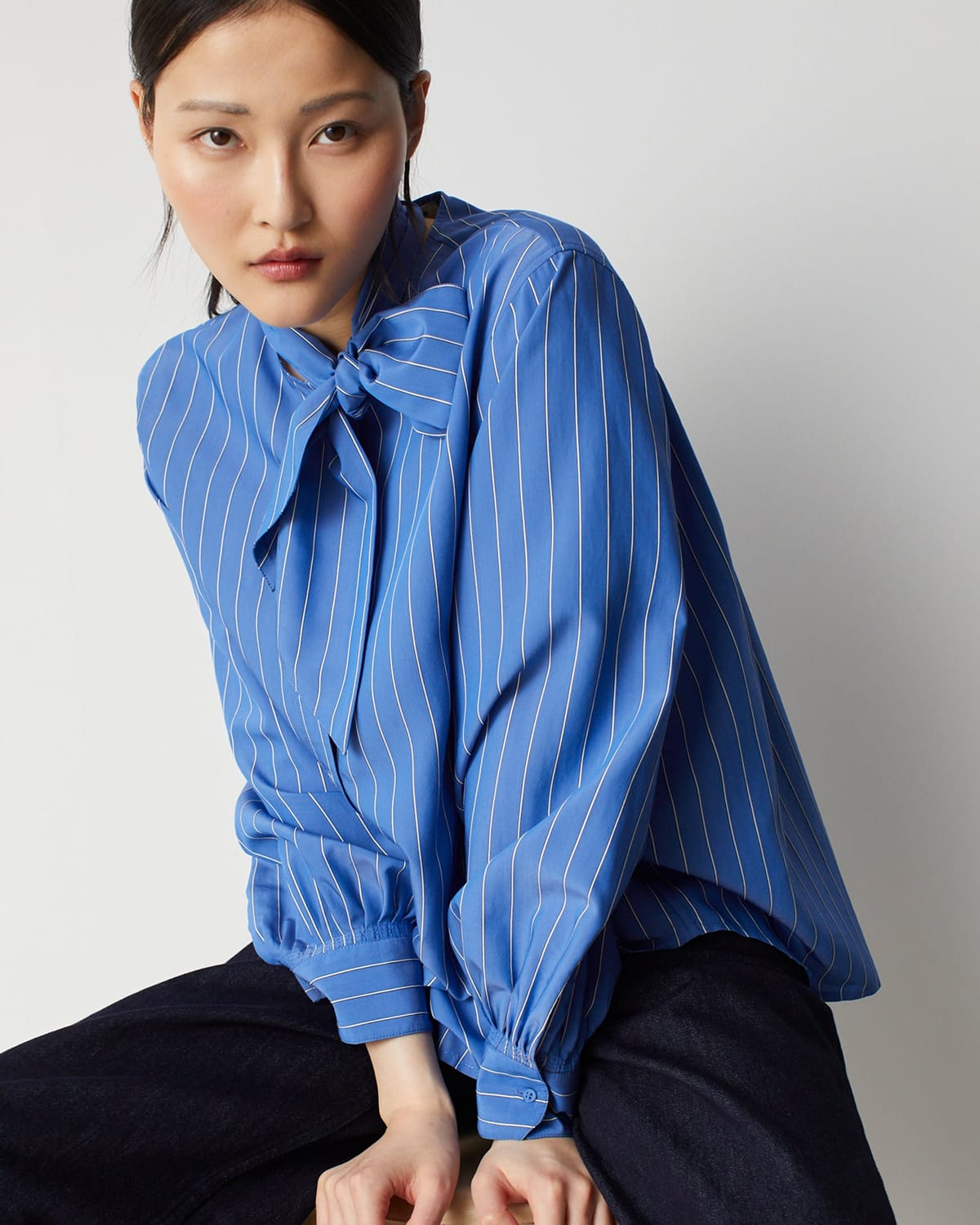 Blouse bleue rayée à col lavallière portée avec un pantalon noir