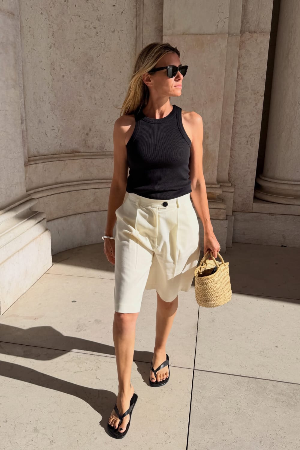Débardeur noir ajusté avec bermuda écru et sandales noires, look d’été minimaliste et tendance.