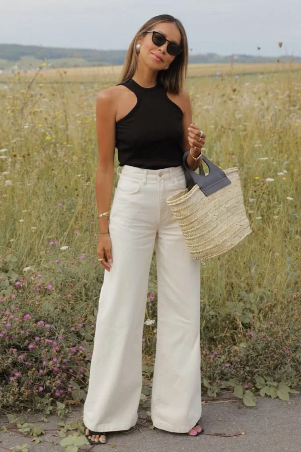 Jean blanc large avec top noir dos nu et panier en paille, silhouette estivale élégante.