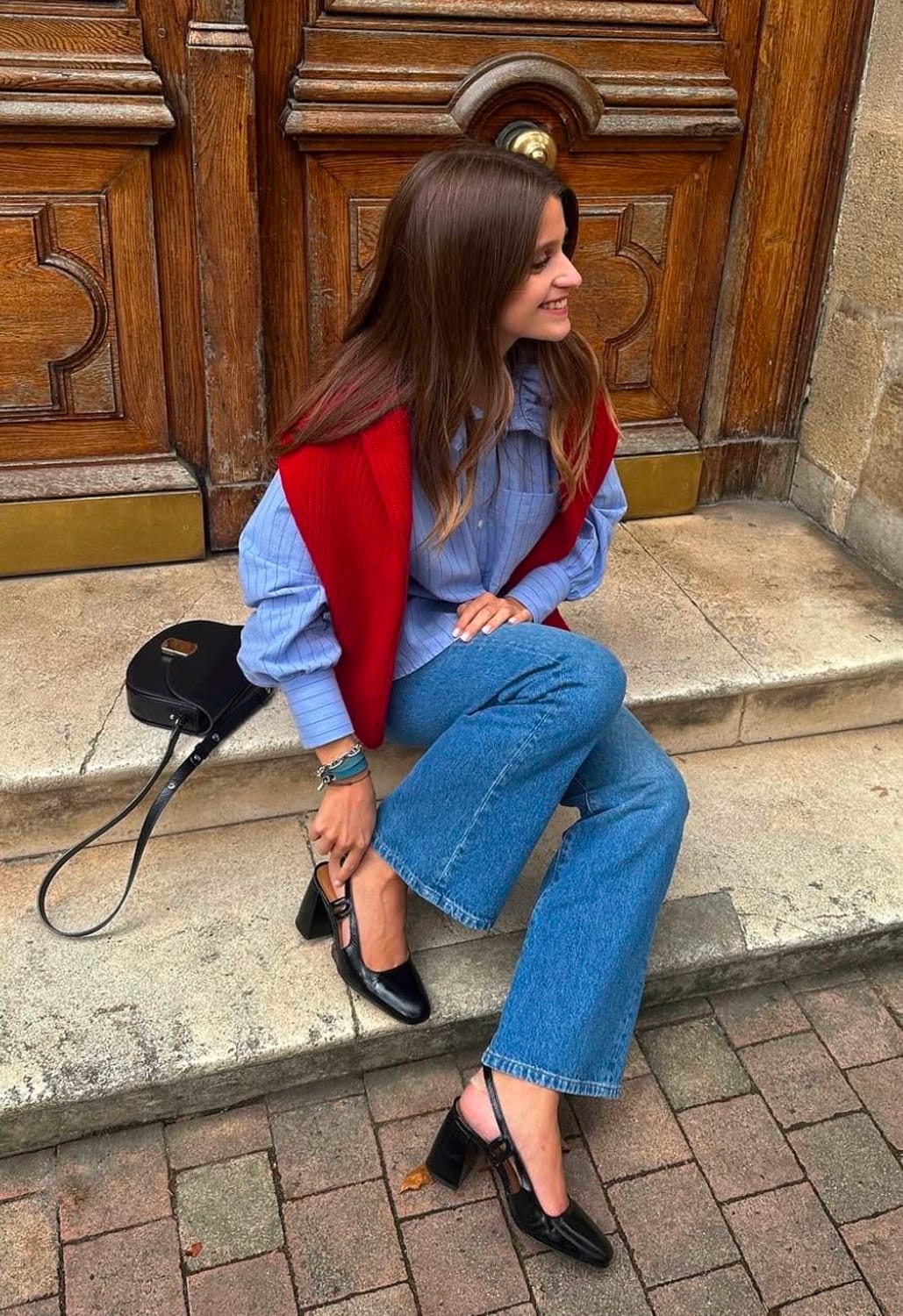 Pull rouge sans manches sur chemise bleu clair avec jean ample et babies noires à talon