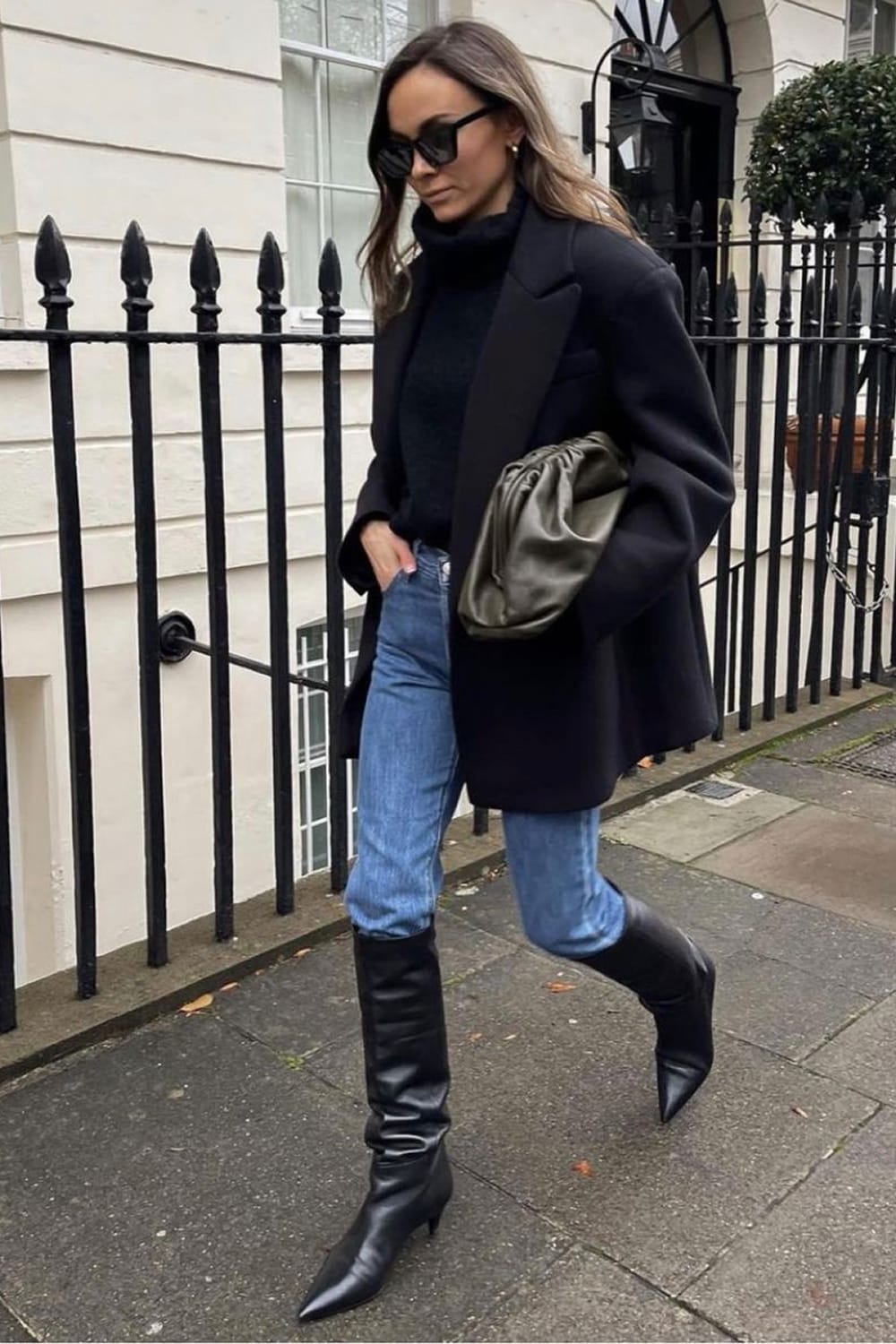 Tendance automne 2026 : jean glissé dans des bottes hautes noires, manteau sombre et sac souple