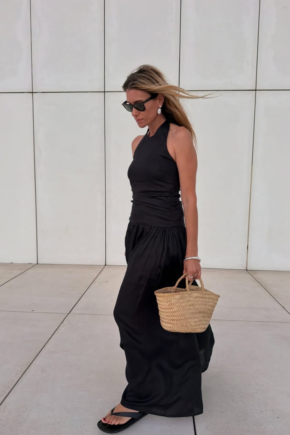 Robe longue noire fluide portée avec un sac en paille et des sandales, look minimaliste pour l’été.