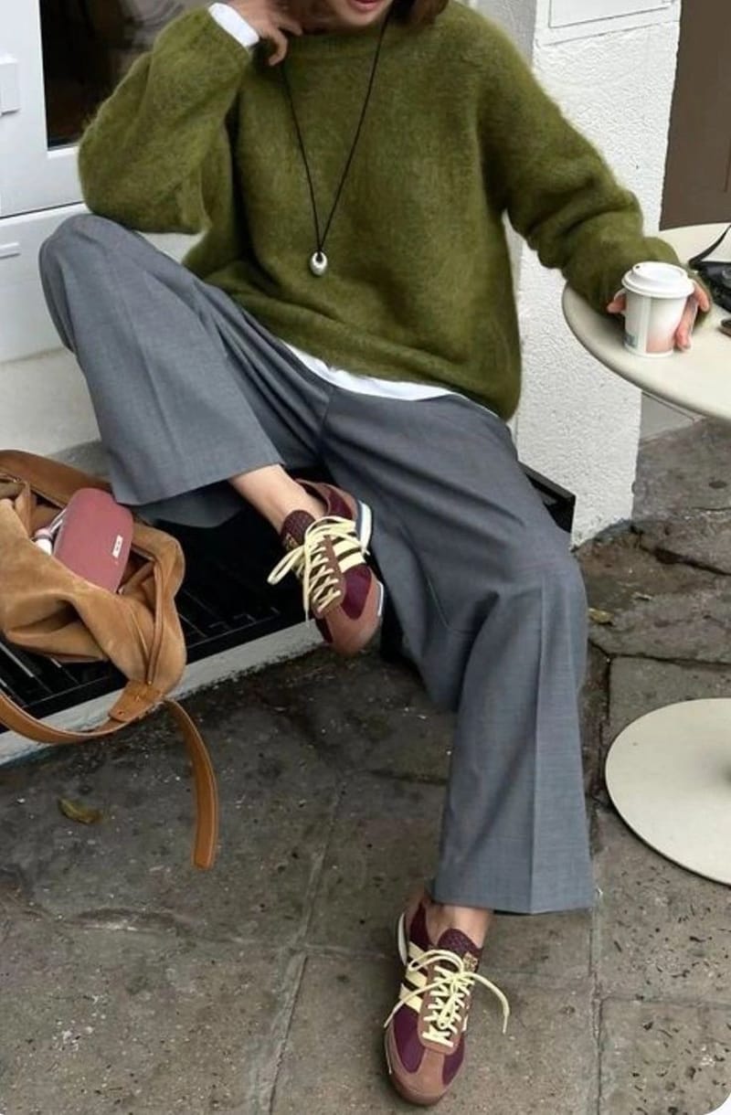 Pull en mohair vert olive sur un pantalon de tailleur gris large, avec des baskets rétro bordeaux et un grand sac en daim camel