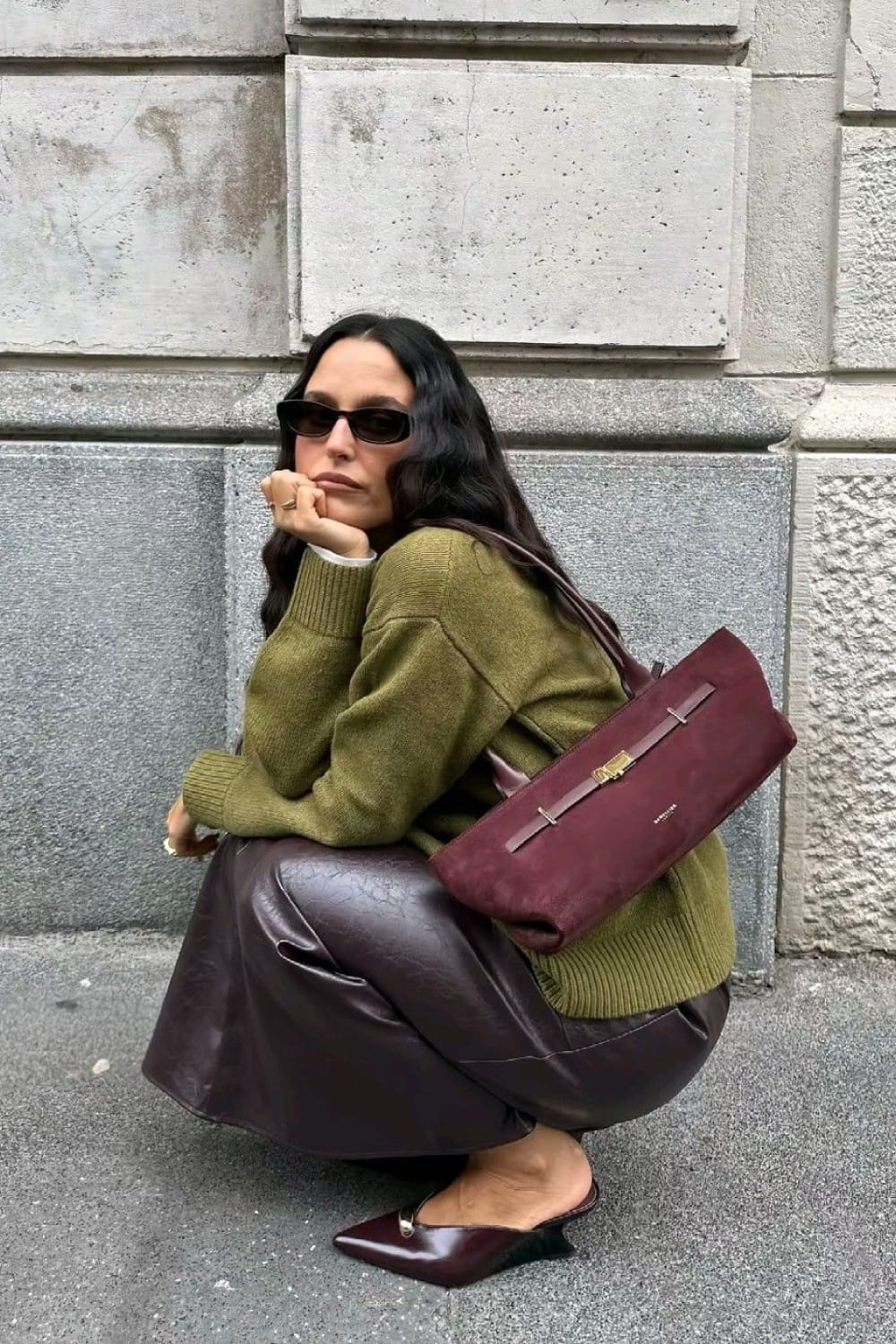 Pull en maille vert olive porté avec une jupe longue en cuir prune, un sac en daim bordeaux et des mules pointues assorties