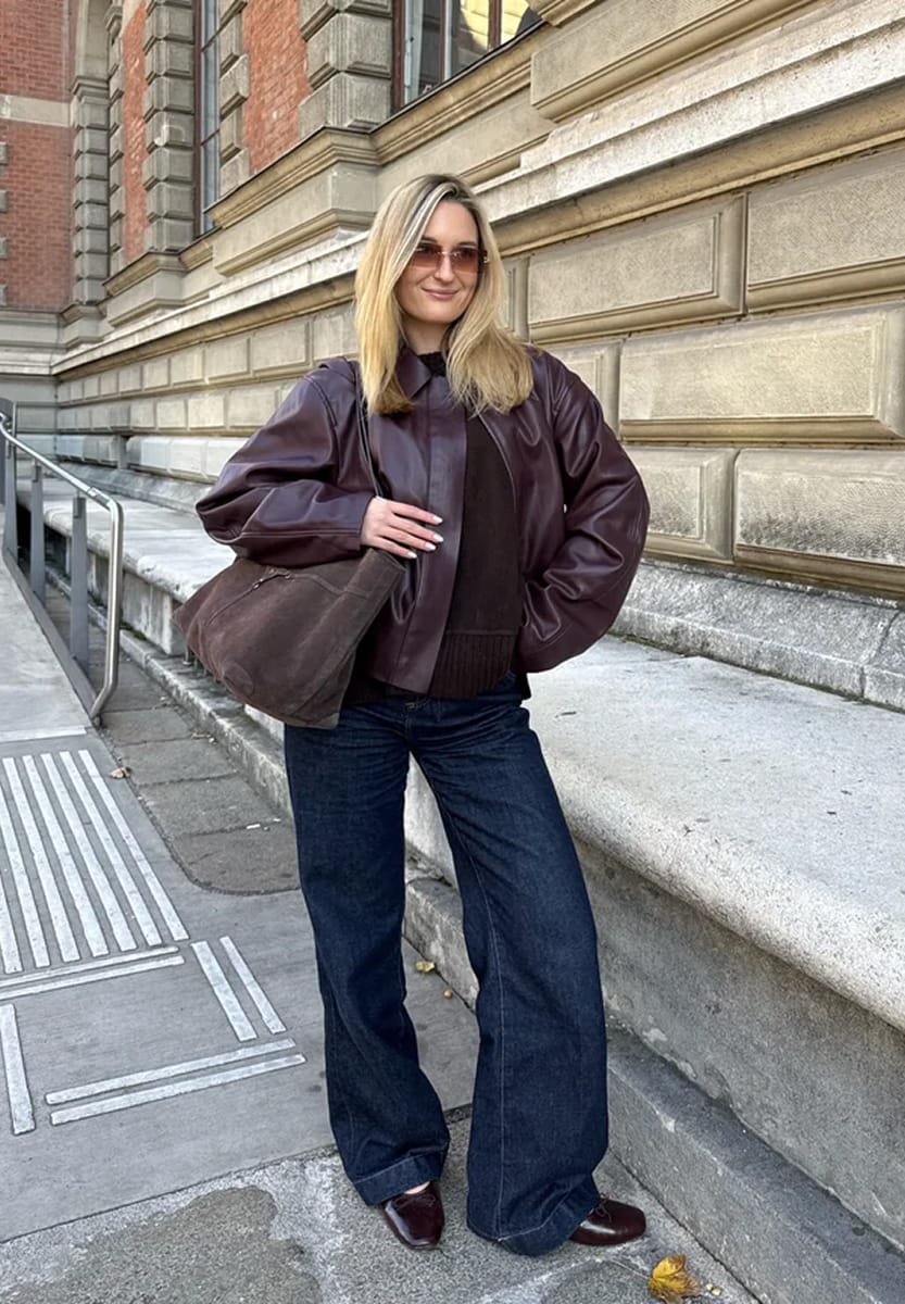 Jean brut large en indigo foncé porté avec un blouson en cuir bordeaux, un sac en daim marron et des mocassins