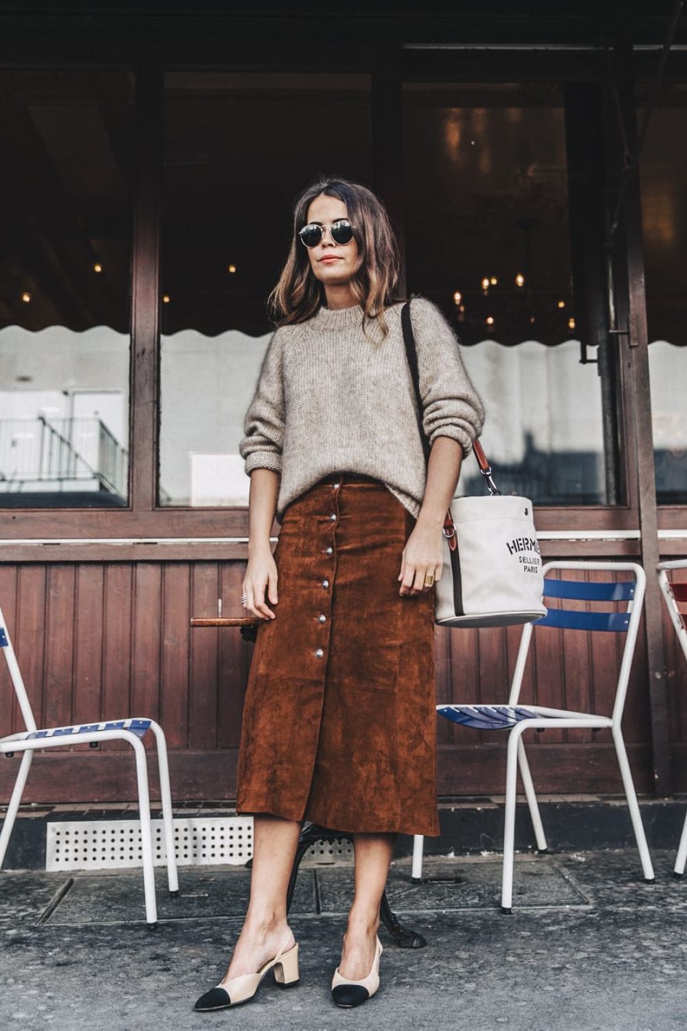 Jupe midi en daim cognac boutonnée devant portée avec un gros pull beige et des escarpins bicolores en automne