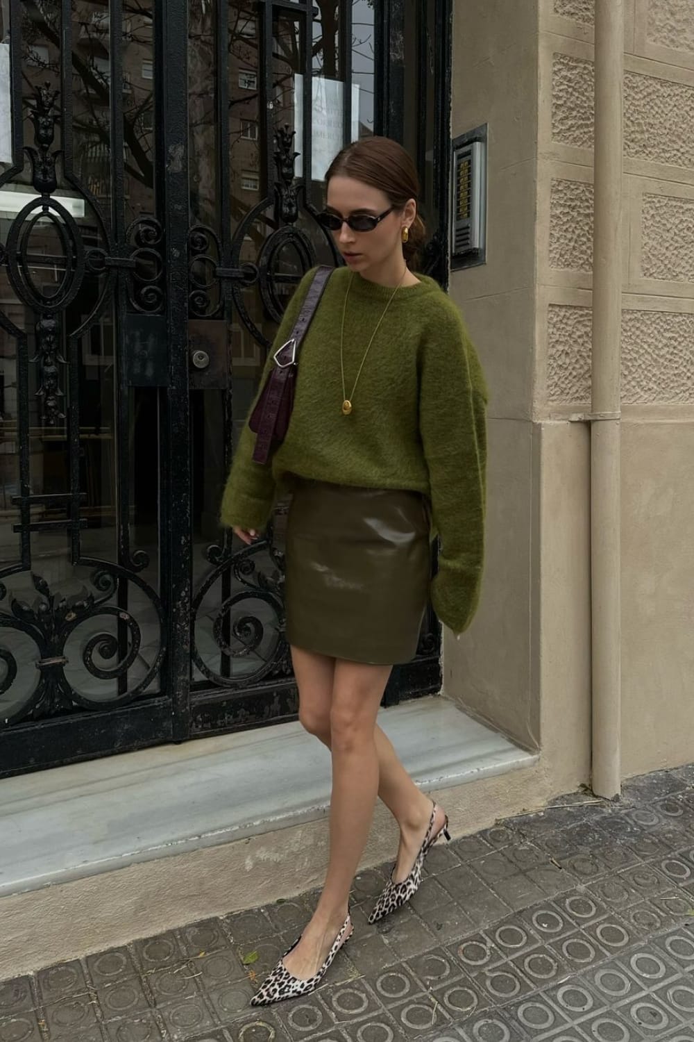 Look monochrome vert olive avec un pull en mohair et une minijupe en cuir kaki, des escarpins à bride léopard et un sac bordeaux