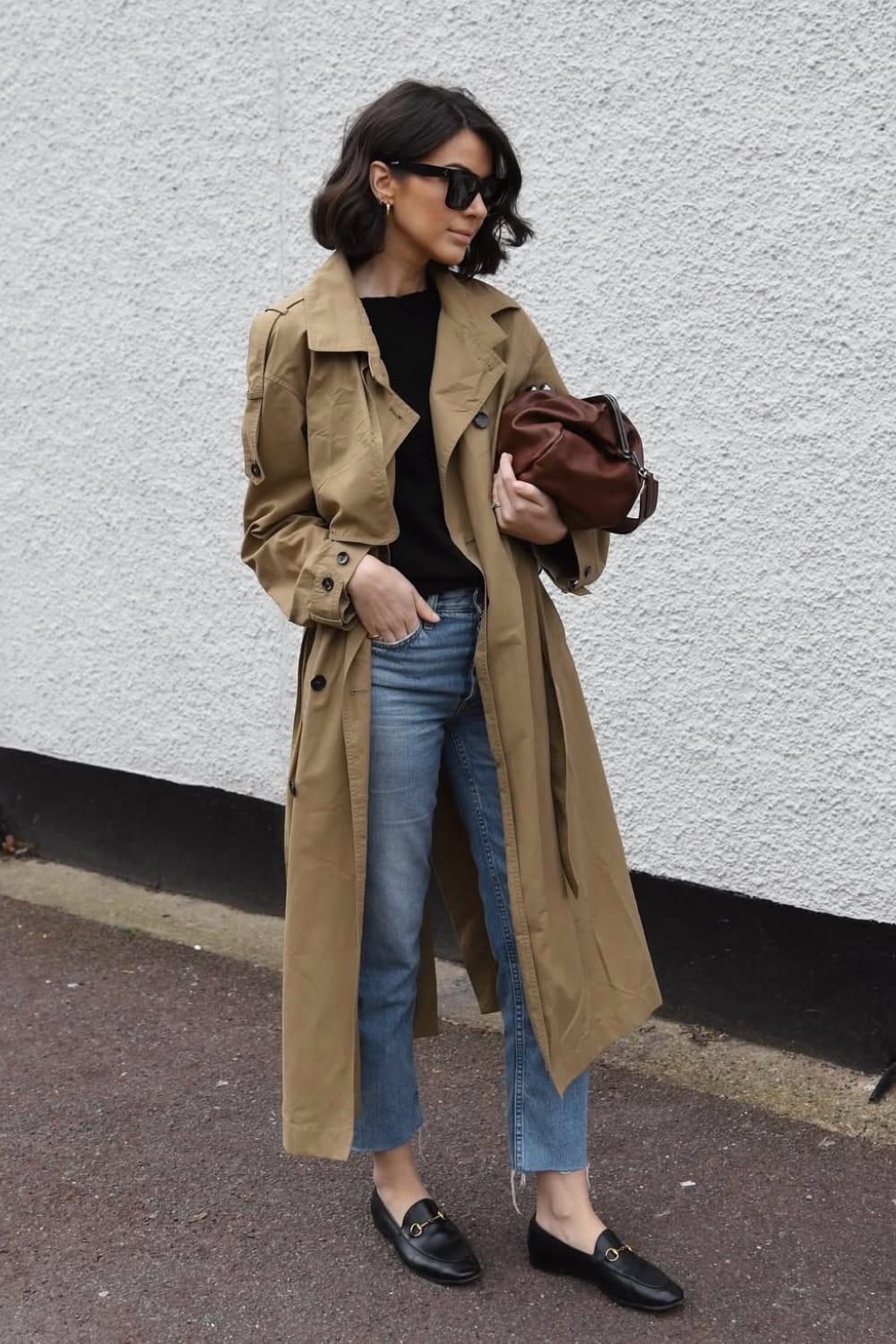 Trench camel porté ouvert avec un pull noir, un jean droit clair et des mocassins noirs à mors en automne