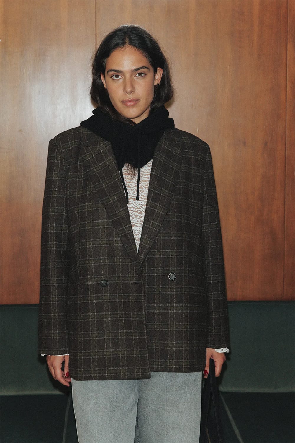Blazer croisé marron à carreaux porté avec un jean clair, un haut écru ajouré et une écharpe noire.