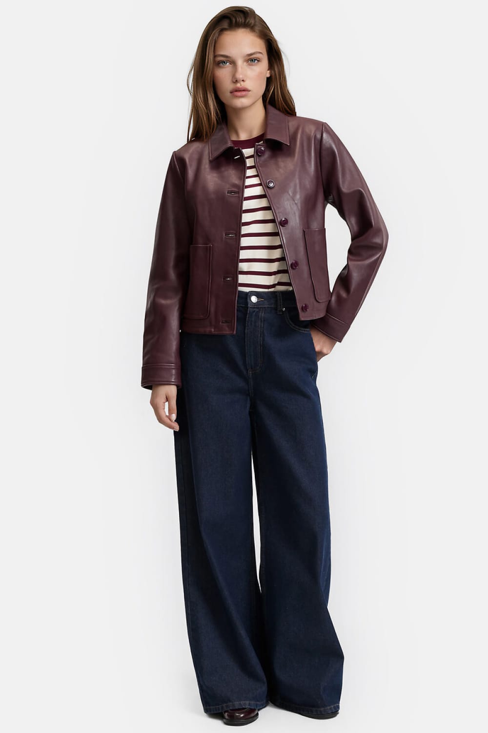 Blouson en cuir bordeaux porté avec un haut à rayures écrues et bordeaux et un jean large bleu foncé.