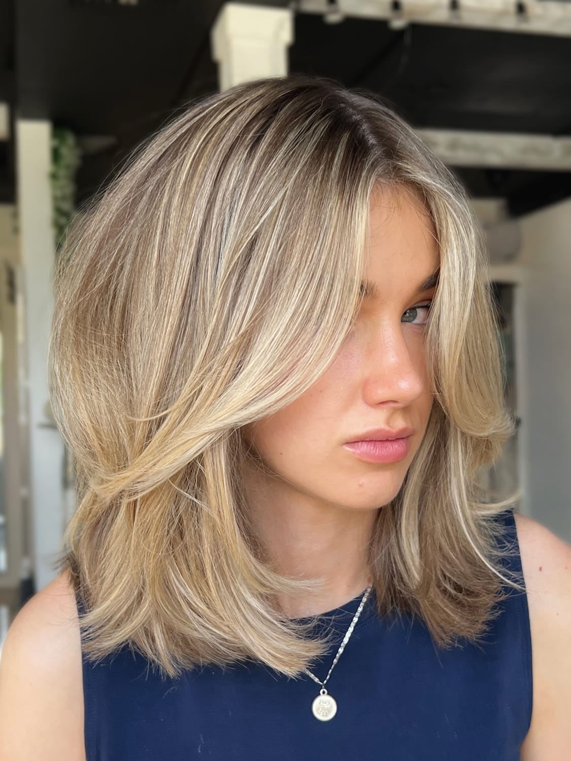 Bob long blond dégradé avec mèches ouvertes autour du visage et pointes arrondies au brushing.