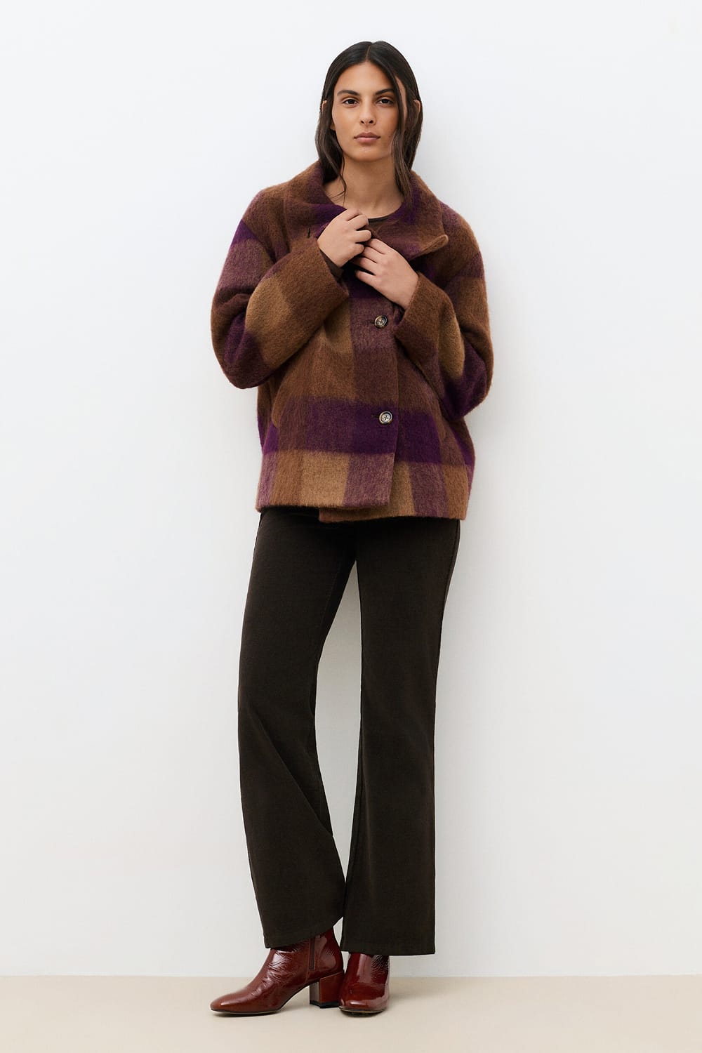 Look de la collection Caroll automne-hiver 2026-2027 : manteau à grands carreaux prune et camel, pantalon large foncé et bottines bordeaux à talon.