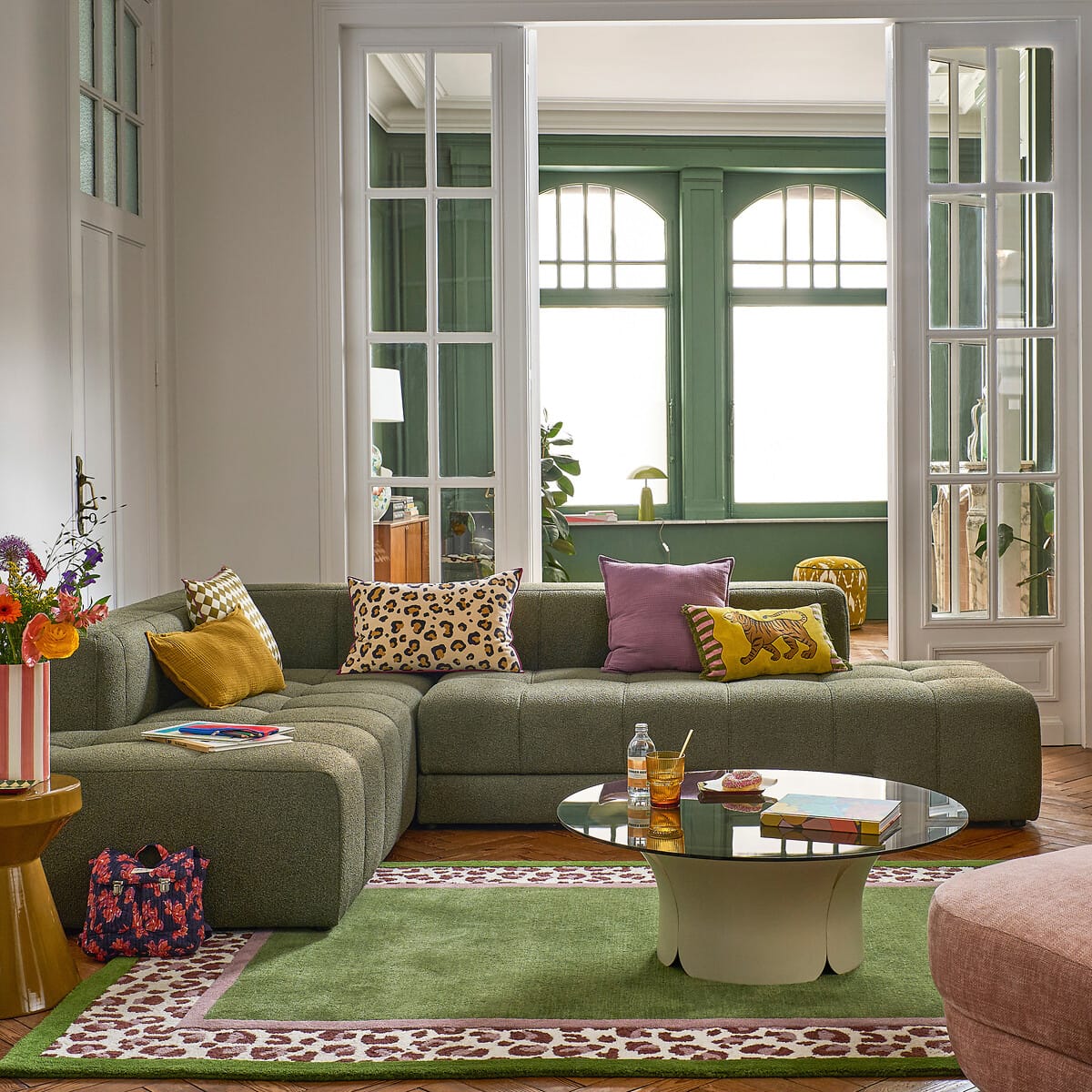 Salon avec canapé d’angle en bouclette verte et tapis en laine vert à bordure imprimé léopard sur parquet en point de Hongrie