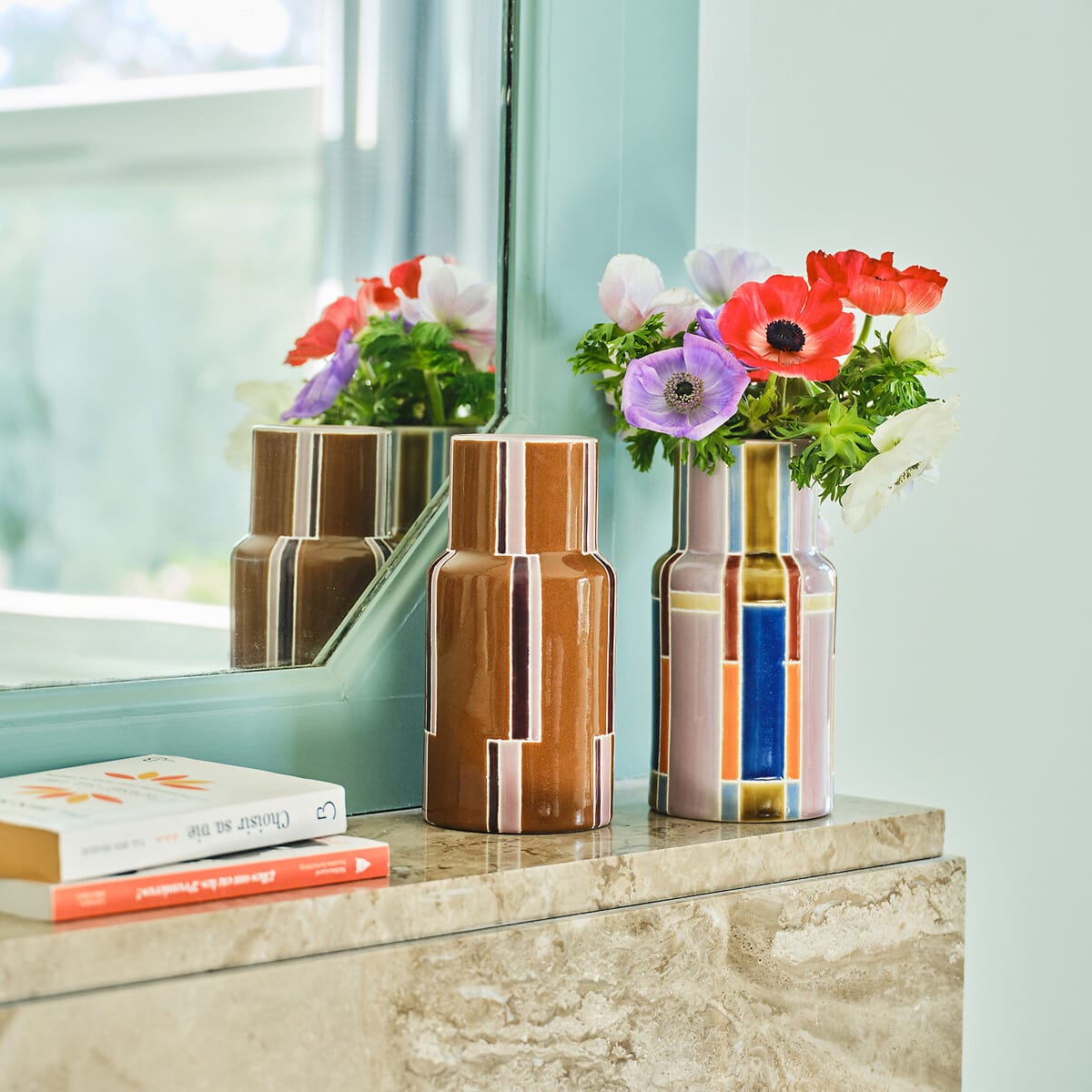 Bouquet d’anémones dans un vase en faïence mauve multicolore SEKMO, posé sur une console en pierre devant un miroir